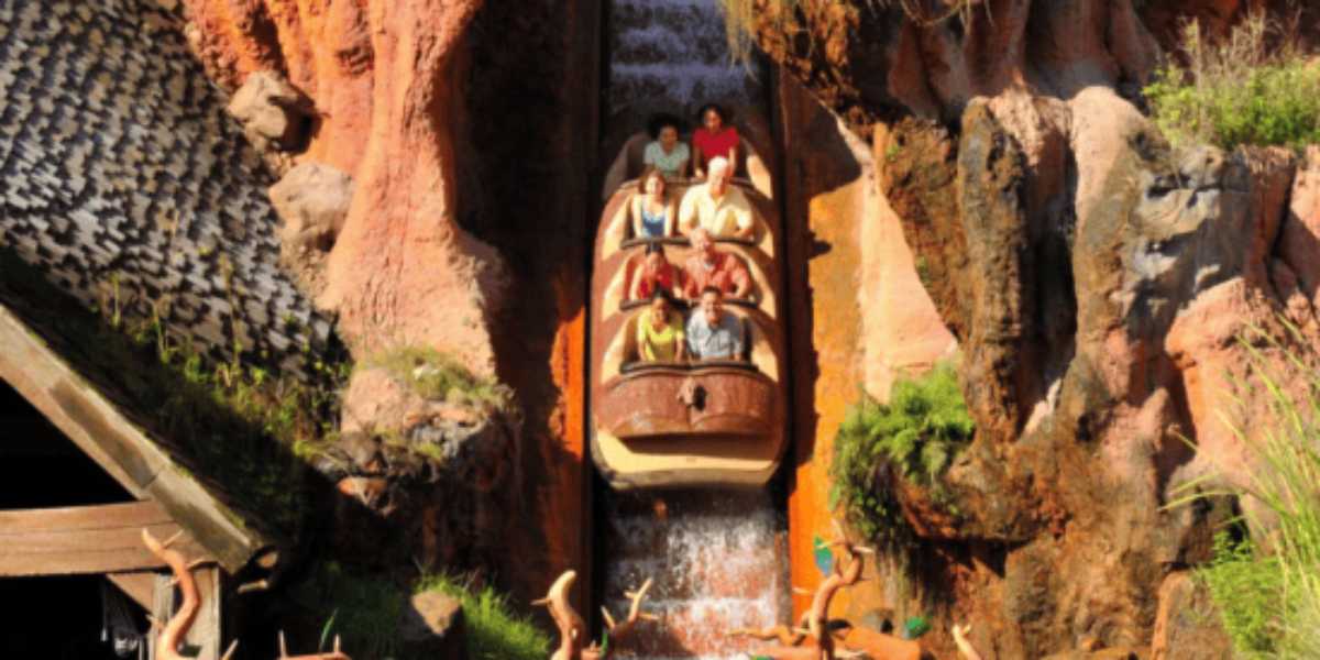 A group of people descend rapidly in Splash Mountain ride amidst a rugged, rocky landscape, splashing water around as they enjoy the thrill.