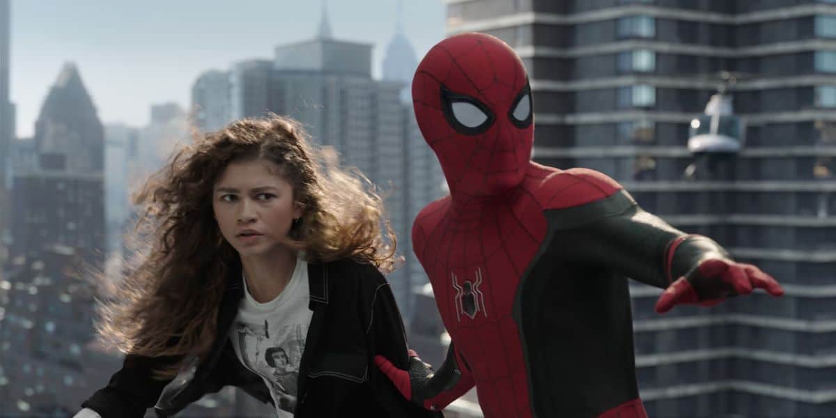 Spider-Man in his red suit and Zendaya as MJ looking anxiously to their side, standing on a building with a cityscape behind them.