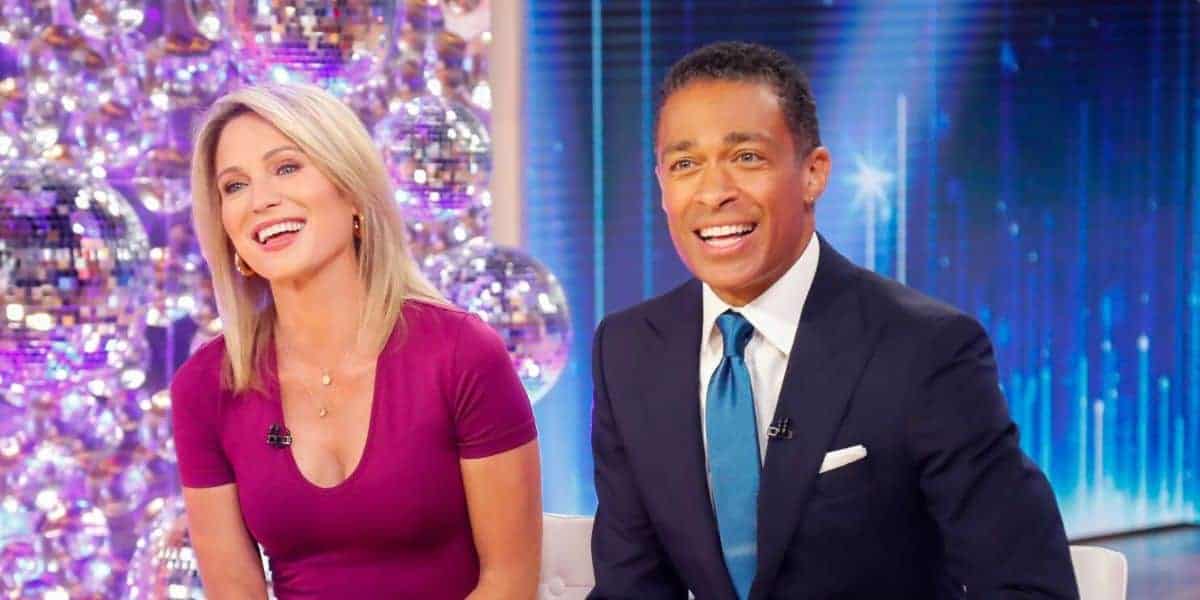 Amy Robach and TJ Holmes sit side by side, smiling, in a brightly-lit studio with a sparkly, festive background. Amy wears a magenta dress while TJ sports a navy suit with a blue tie. Both look towards the camera, exuding a joyful and engaging presence.