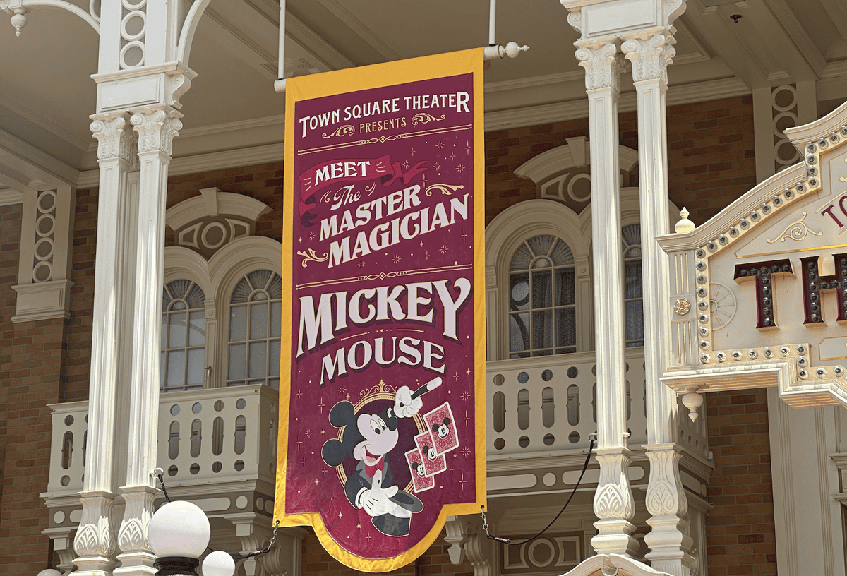 A banner outside the town square theater announcing a meeting with mickey mouse, titled "the master magician," featuring an illustration of mickey in a magician's outfit.