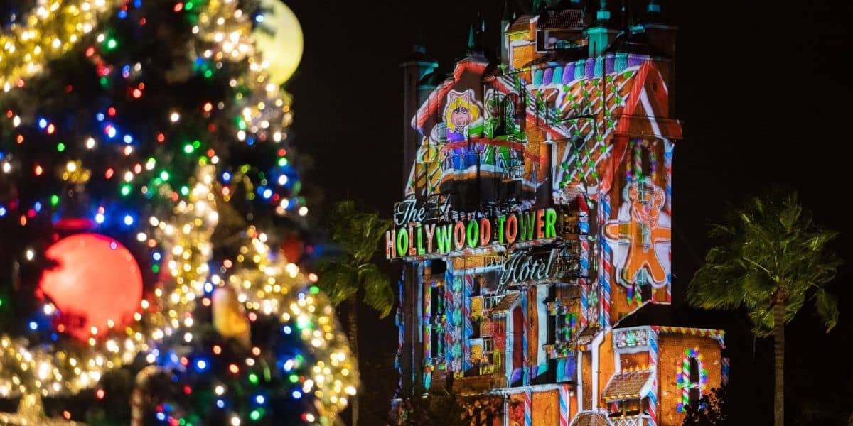 A colorful, decorated Christmas tree is in the foreground, while the illuminated Hollywood Tower Hotel is in the background.