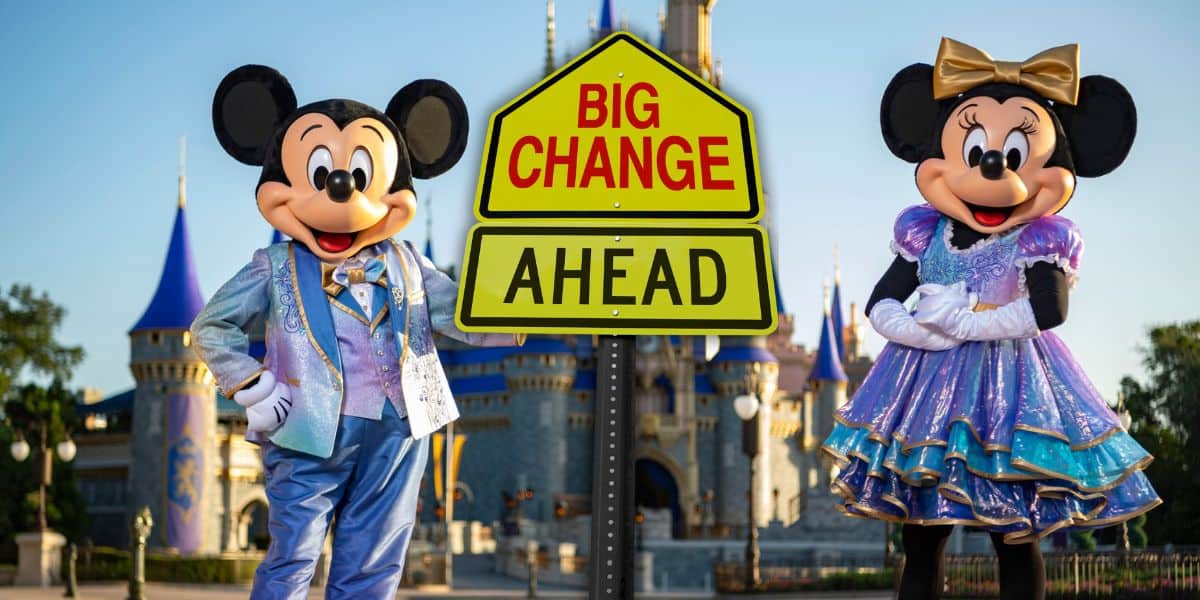 Mickey Mouse and Minnie Mouse stand on either side of a yellow road sign that reads "Big Change Ahead." Both characters are dressed in festive, sparkling outfits. A castle with blue and gold accents is visible in the background, suggesting a Disney theme park setting.