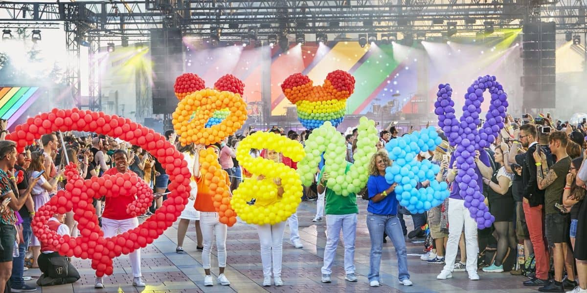 A group of people hold large balloon letters spelling "Disney" in various bright colors.