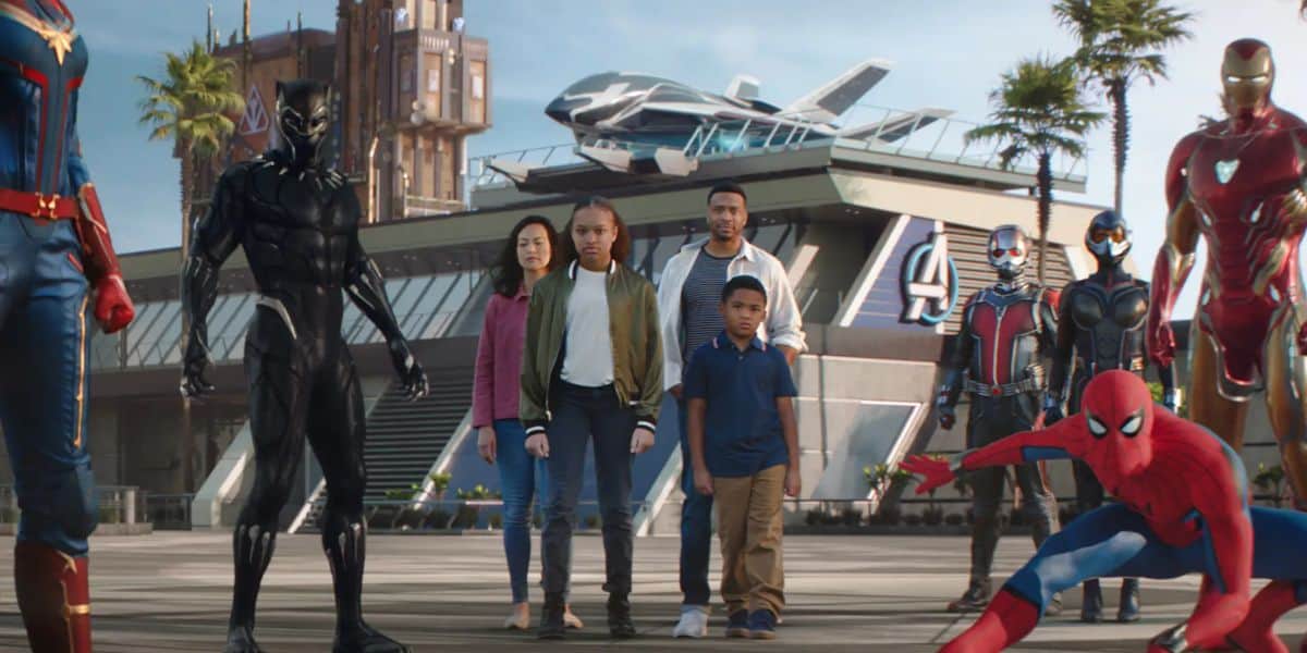 A group of Marvel superheroes, including Black Panther, Iron Man, Spider-Man, Captain Marvel, and Ant-Man, pose with a family in front of a futuristic Avengers headquarters at Disney California Adventure Park.