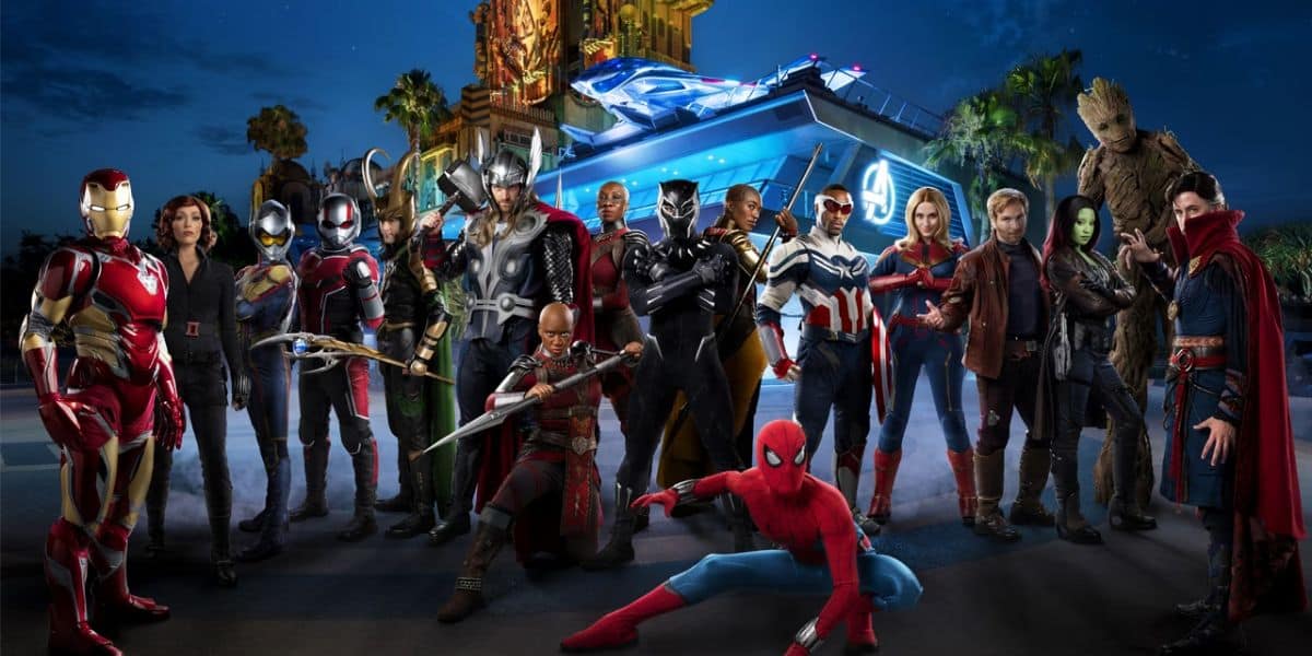 A group of Marvel superheroes, including Iron Man, Black Widow, Ant-Man, Thor, Black Panther, Spider-Man, and others, stand in dynamic poses in front of a futuristic building resembling the Avengers headquarters at a Disney park. The scene is set at twilight and promises entertainment for all ages.