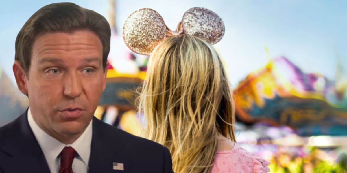 A man in a suit, who appears to be in the foreground, looks to the left with a concerned expression. In the background, a person with long blonde hair wears glittery mouse ears, facing away towards colorful amusement park rides.