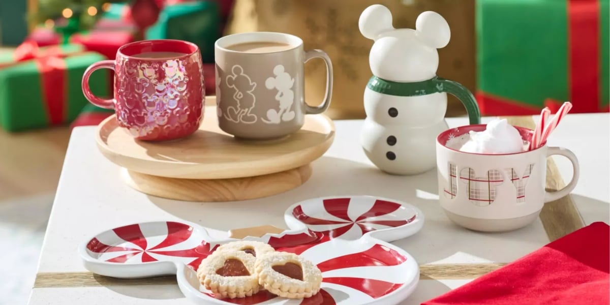 A festive setup with holiday-themed mugs from the enchanting collection, including one with a snowman handle, cookies on peppermint-shaped plates, and presents in the background. One mug holds hot chocolate with whipped cream and candy canes.