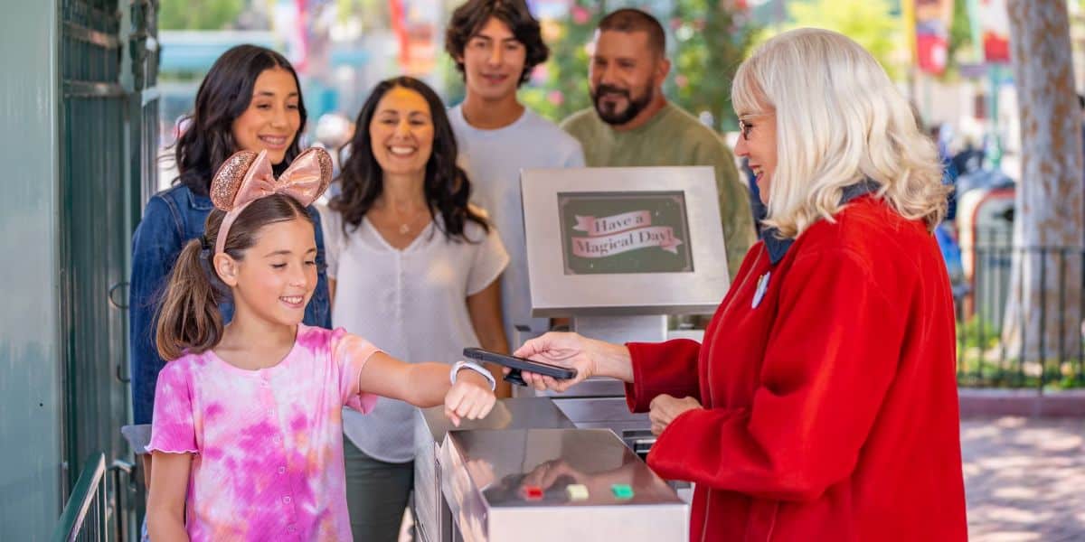 A family of five uses Magicbands to scan into Disneyland Resort at the gates, assisted by Disney cast members.