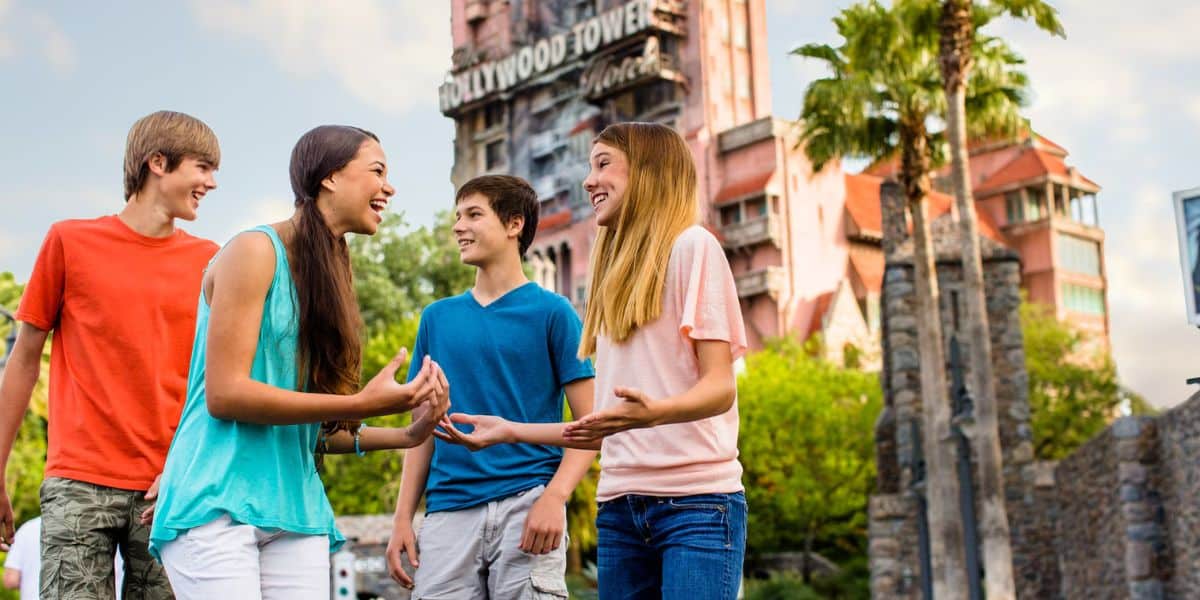 Four teenagers laughing and talking in front of the twilight zone tower of terror attraction in Disney's Hollywood Studios theme park on a sunny day.