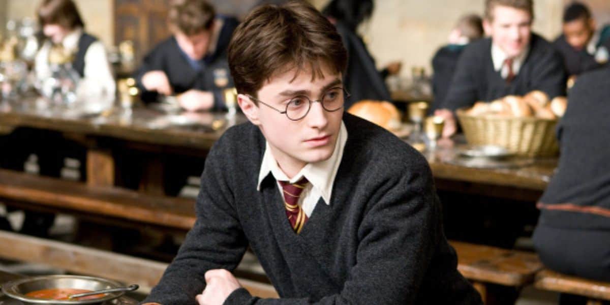 Harry potter, wearing Gryffindor robes and glasses, sits at a table in the Hogwarts dining hall.