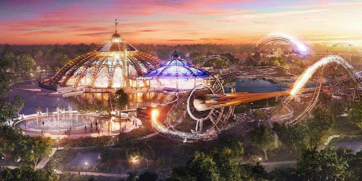 A vibrant amusement park at sunset, part of the Epic Universe, features a dome-covered carousel with colorful lights. Nearby, a roller coaster with a fiery design spirals around, emitting sparks. People enjoy fountains and lush greenery surrounds the attractions.