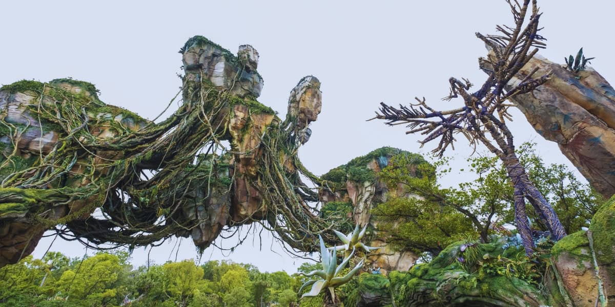 The image shows an otherworldly landscape with floating rock formations covered in lush green foliage and intertwined with thick vines. A tall, twisted tree-like structure is also visible, enhancing the surreal atmosphere. The sky is clear and bright.