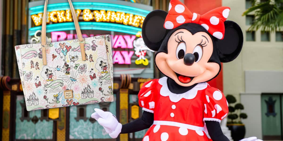 Minnie Mouse, in her red polka dot dress and bow, stands beside a Disney Whimsy Sketch Tote by Dooney & Bourke. The handbag brims with Disney characters and charm, while a vibrant sign with lights glows in the background.