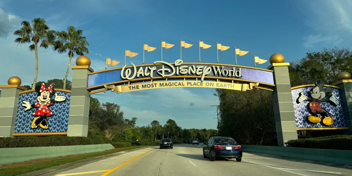 The WDW entrance sign as cars drive underneath on a summer day. 