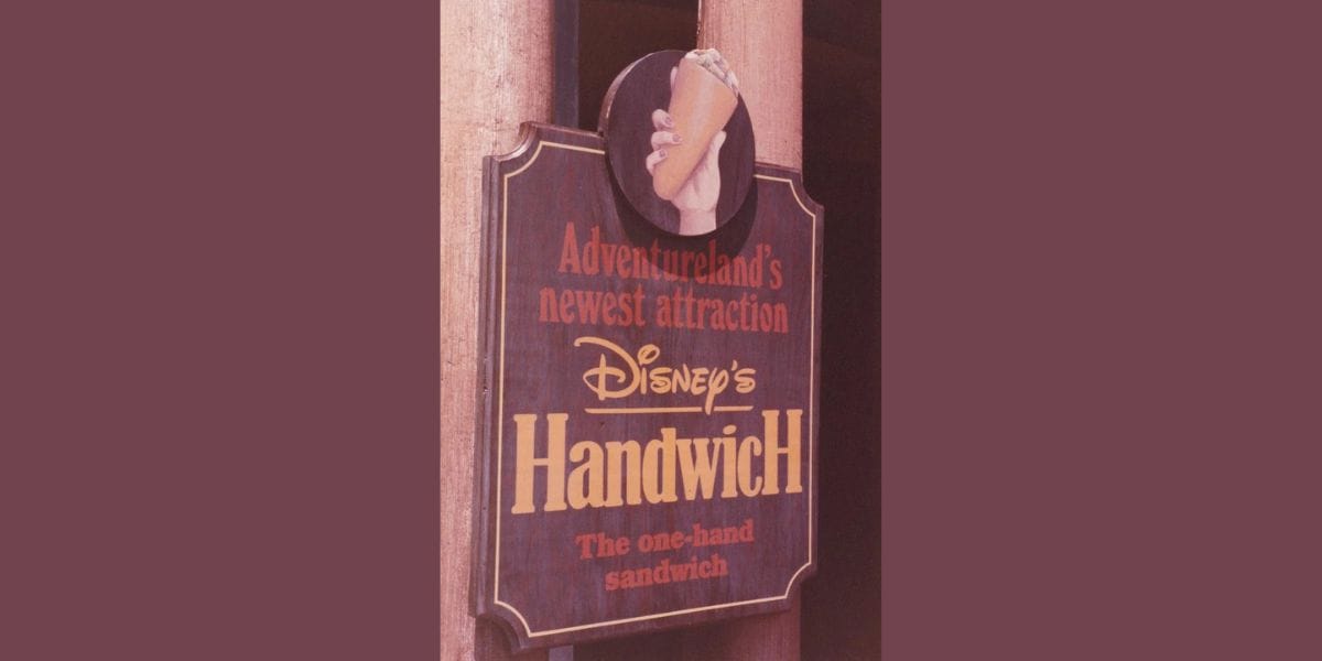 Sign for "Disney's Handwich" in Disney World Adventureland, advertising a bizarre sandwich that can be held with one hand. The image features text that emphasizes the novelty of this unique attraction.