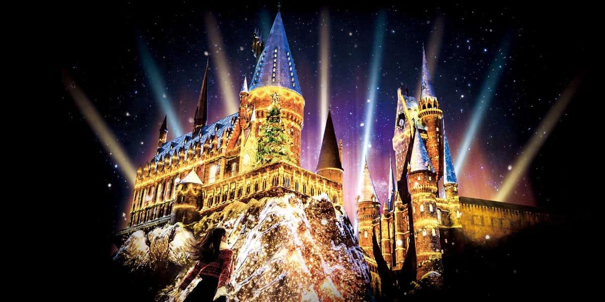 Multicolored light beams illuminate Hogwarts Castle at night under a starry sky, creating a magical and mystical ambiance.