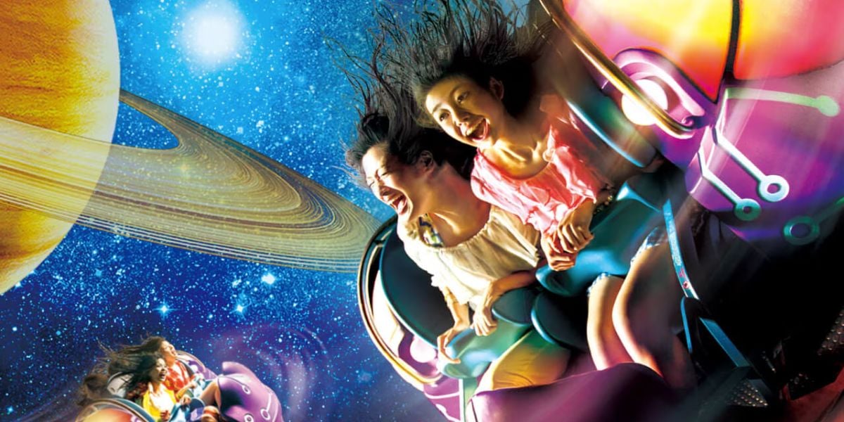 Two people enjoy a thrilling ride on Universal Studios' beloved roller coaster with a space theme. Their hair is blown back as they smile, surrounded by imagery of stars and a planet with rings, creating a sense of excitement and adventure.