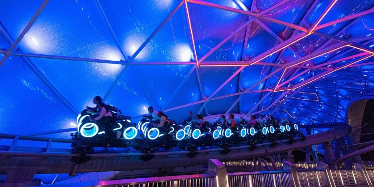 Experience a futuristic roller coaster with riders on motorcycle-style vehicles inside a dome lit with blue and pink lights, creating a glowing and dynamic atmosphere. Secure your spot effortlessly through the virtual queue for an unforgettable adventure.