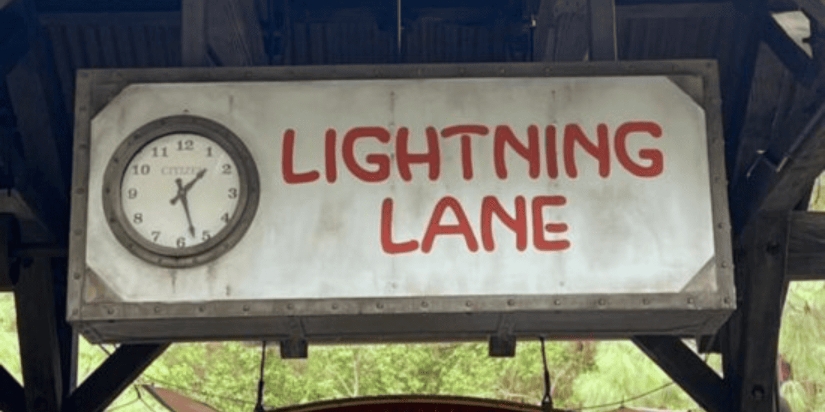 A sign that reads "lightning lane" in red letters on a white background. A clock is positioned next to the sign. This entrance also services those who use a Disney Das Pass.