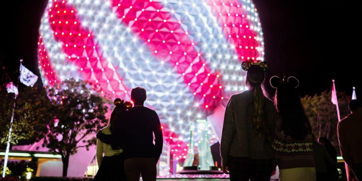 A night scene showing the back view of a family wearing Mickey Mouse hats, gazing at the illuminated Spaceship Earth at EPCOT.