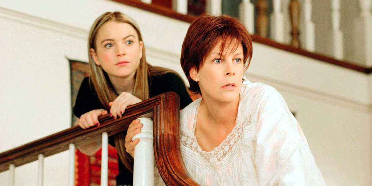 A young woman with long blonde hair and a concerned expression leans on a staircase railing, looking forward. Beside her, an older woman with short reddish-brown hair, also with a worried look, is dressed in white pajamas and holds the railing with both hands—two major characters returning for Freaky Friday 2.