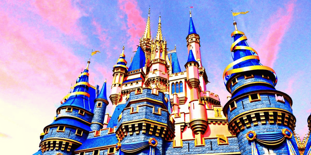 A brightly colored Cinderella castle with blue and gold conical roofs and ornate spires, framed by a vibrant pink and blue sky. The castle exudes the Magic Kingdom’s whimsical and magical ambiance at Disney World.