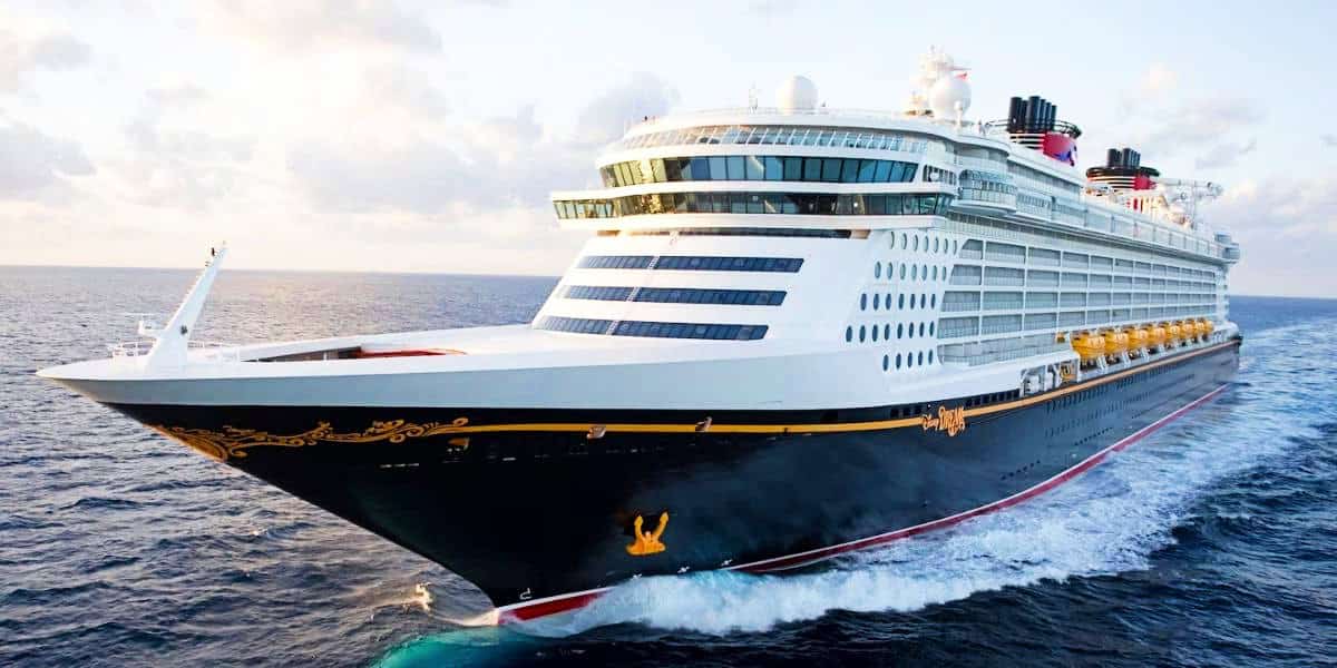 Disney Dream ship, adorned with elegant golden designs, sails on the open ocean under a clear sky, showcasing its vast scale and modern structure.