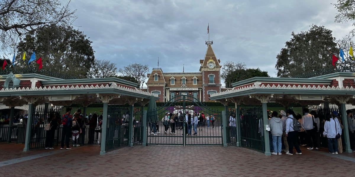 A large crowd of guests in line outside the gates waiting to enter Disneyland Park in Southern California with the Main Street station of the Disneyland Railroad in the background