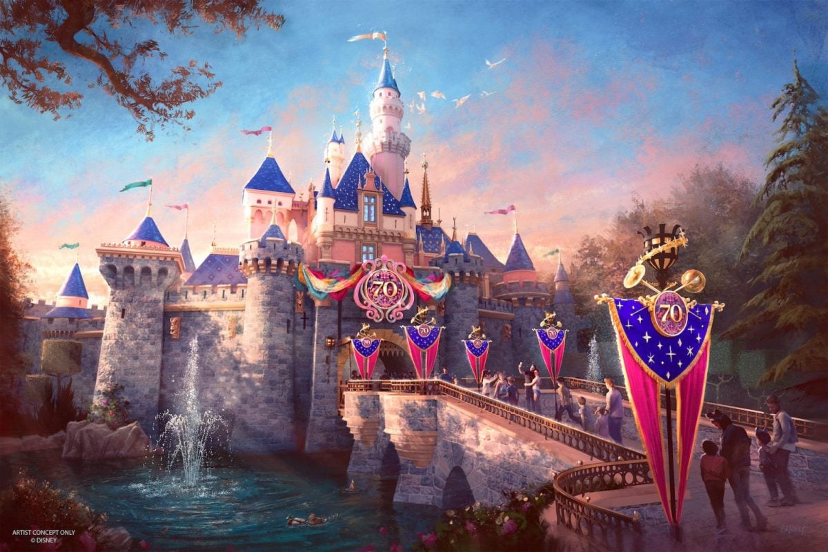 A whimsical castle adorned with "70" anniversary banners, featuring pink and blue towers reminiscent of Disney Park (Disneyland's) magic. People gather for a Meet-N-Greet near a fountain by the entrance. The scene is illuminated by a warm, golden sunset with birds flying above.