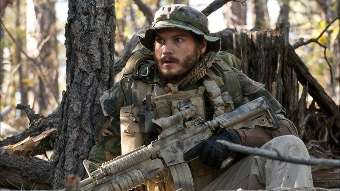 A soldier in camouflage gear and helmet crouches in a forest, gripping a rifle and looking alert. The scene evokes intense realism, reminiscent of National Geographic’s storytelling—unrelated to the Disney National Geographic lawsuit coverage.