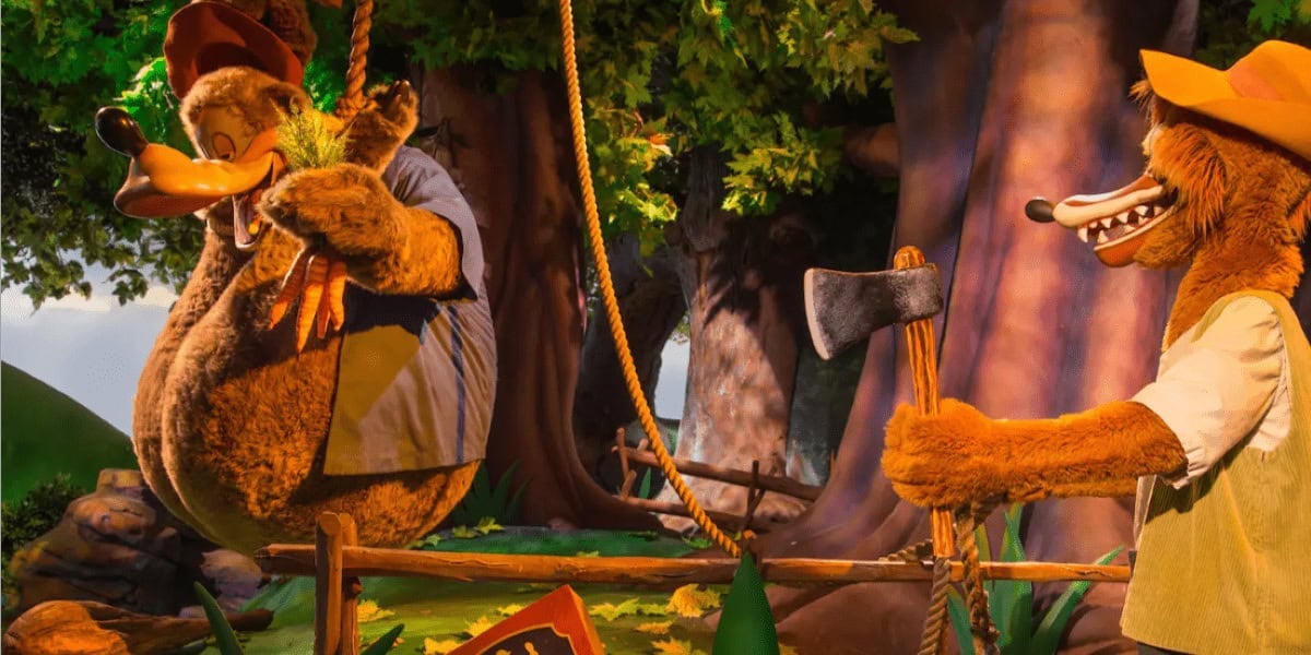 Animatronic figures of a bear and a fox bring the Splash Mountain returning vibe to life in a forest scene. The bear sits on a rope swing attached to a tree, while the fox stands nearby holding an axe, surrounded by trees and a wooden fence.