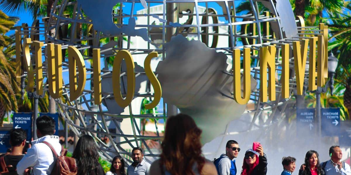 The entrance of Universal Studios Hollywood, featuring a rotating globe surrounded by a metal structure with the park's name, as visitors walk towards the entrance.