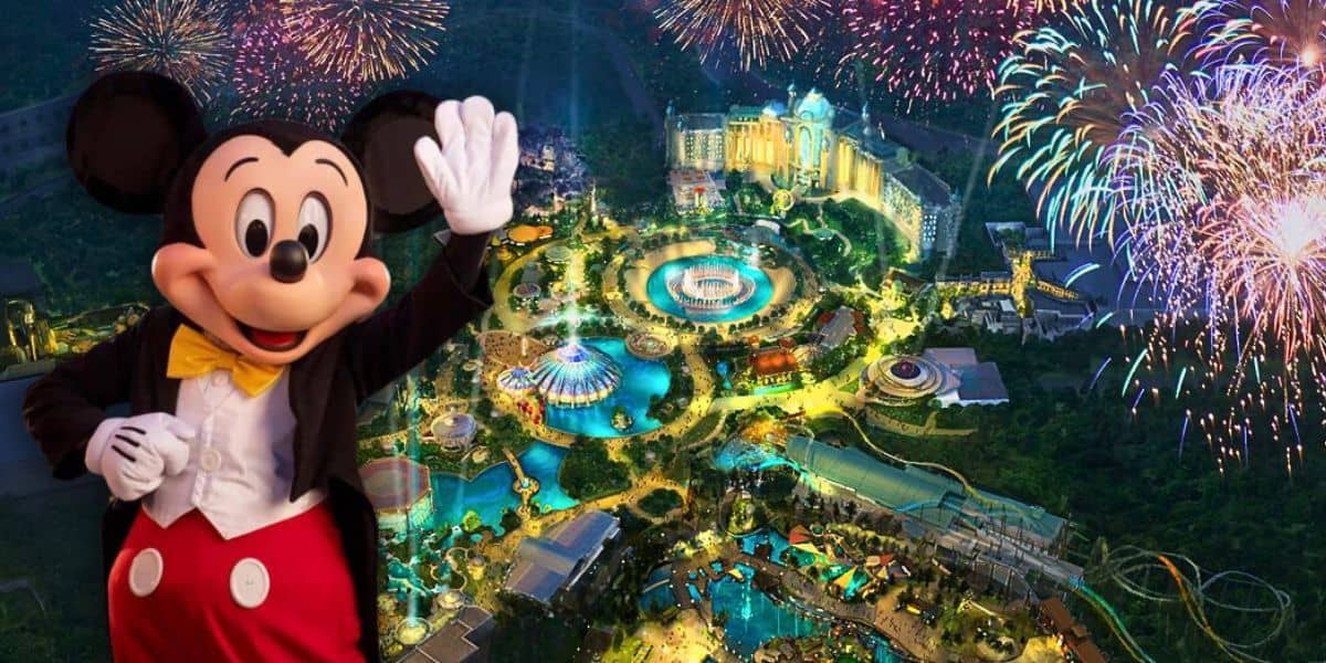 Mickey Mouse waves in front of a vibrant aerial view of Disney World at night, where colorful fireworks illuminate the sky. In the distance, various attractions and structures shimmer below, a reminiscent spark as the Disney Universal Epic Universe theme park gets stronger.