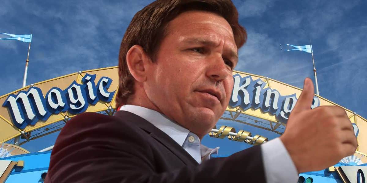 Ron DeSantis giving a thumbs up in front of the Magic Kingdom entrance sign under a blue sky at Disney World.
