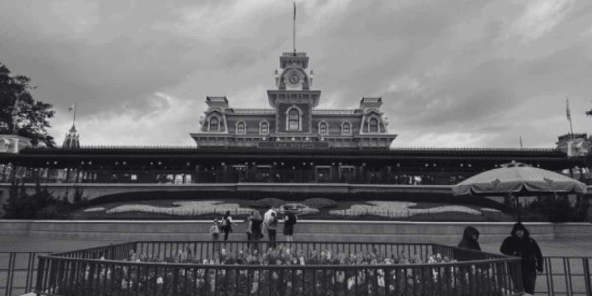 A black and white image of the entrance to Magic Kingdom Park, including the Main Street, U.S.A. train station near the Magic Kingdom ferry.