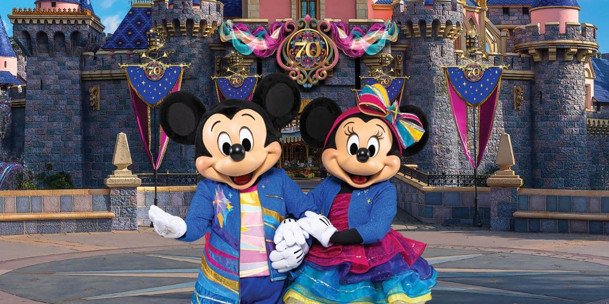 Mickey Mouse and Minnie stand in front of a castle adorned with Disneyland70 decor.