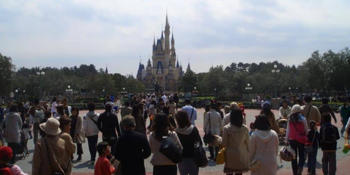 A large crowd of Disney fans walks towards Cinderella Castle at Tokyo Disneyland