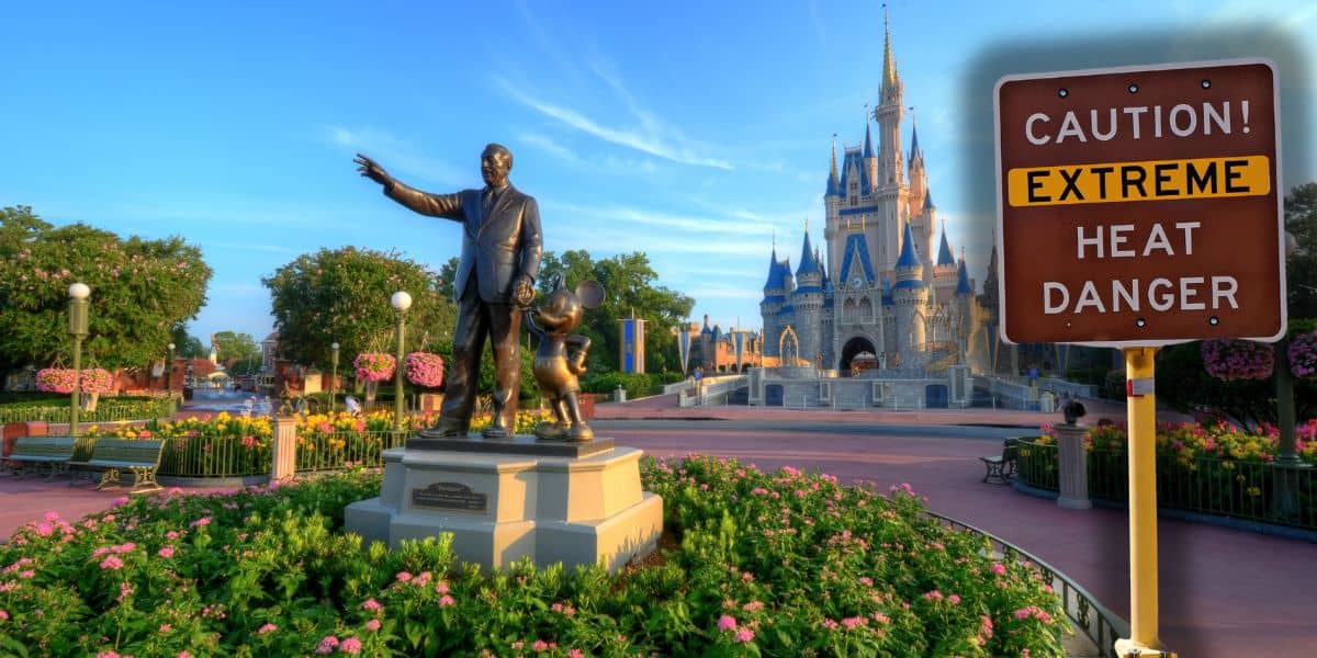 A statue of a man and a mouse stands in a garden near a castle, with clear blue skies overhead. A sign nearby reads "CAUTION! EXTREME HEAT DANGER," indicating potential weather hazards in the area. The scene has that magical Disney theme park charm.