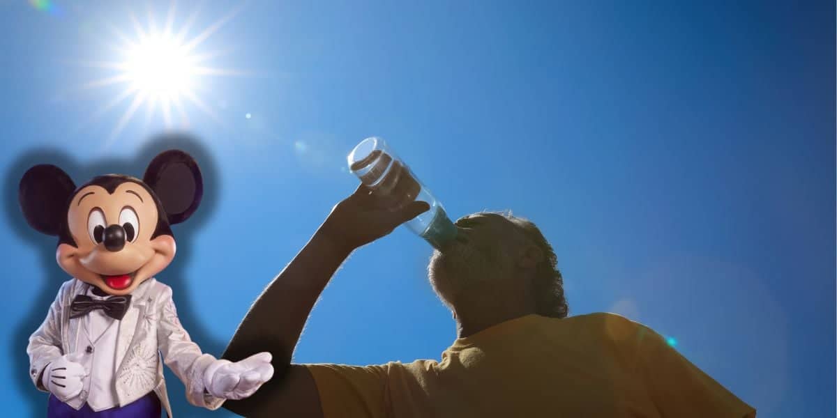 A person dressed in a yellow shirt is drinking water from a glass under a bright, sunny sky with the sun directly overhead. Battling the scorching heat wave, a Mickey Mouse mascot in a white suit and black bow tie stands to the left, smiling at Disney guests while they try to stay cool.