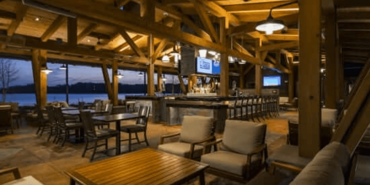 Brown wooden beams throughout an empty restaurant with brown wooden tables and green pillowed chairs.