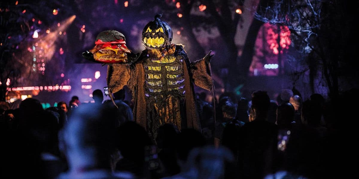 A pumpkin scarecrow holding a burger as a crowd looks on during Halloween Horror Nights at Universal Orlando Resort