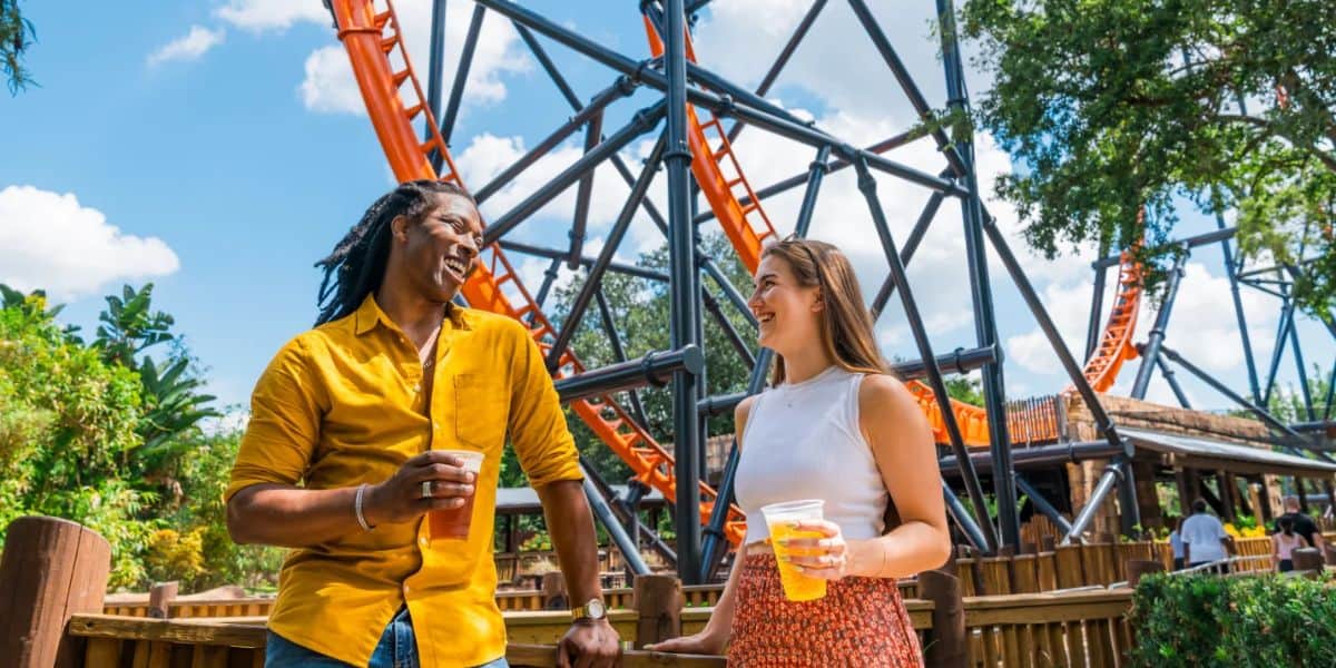 A man and a woman enjoy drinks while standing in front of a roller coaster at Busch Gardens Tampa Bay, a Florida theme park.
