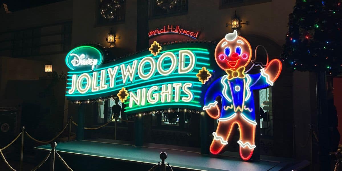 A brightly lit neon sign reads "Disney Jollywood Nights" with a large gingerbread man in a blue outfit and yellow bow tie.