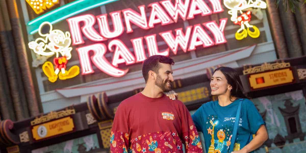 Guests wearing Jollywood Nights merchandise in front of Mickey & Minnie's Runaway Railway