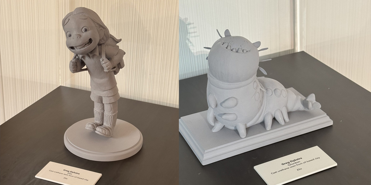 Two gray clay sculptures are displayed on black tables. The left sculpture is of a smiling child with a backpack. The right, inspired by Elio, features a creature with a large head and spiky back—adding an Around the World charm to the scene. Each has a label in front.