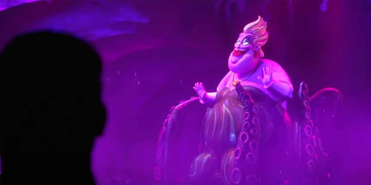 A silhouette watches an animated scene from The Little Mermaid—a purple-skinned, white-haired villain with outstretched tentacles set in a glowing, underwater world—capturing the magic of this Hollywood Studios musical adventure.