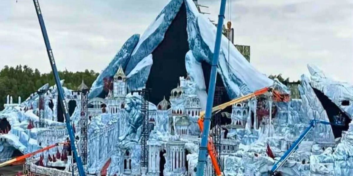 Large outdoor stage set resembling an icy mountain and frozen palace, surrounded by cranes and construction equipment, with a cloudy sky and trees in the background at Tomorrowland Festival, similar to the same named Magic Kingdom land.