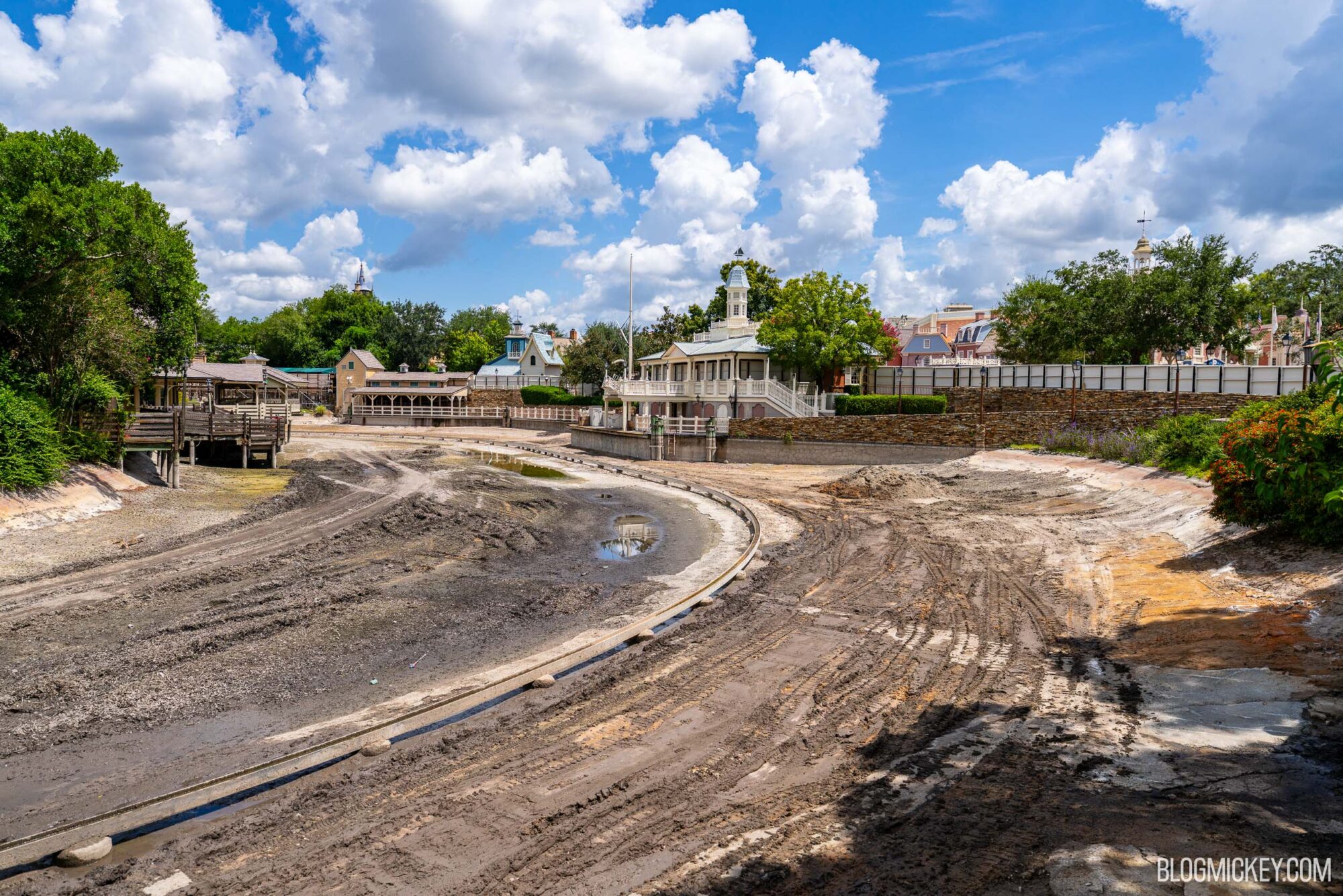 Drained Rivers of America with exposed ride track. A lush Tom Sawyer Island sits on the other side of the drained river basin and Liberty Square is visible in the distance