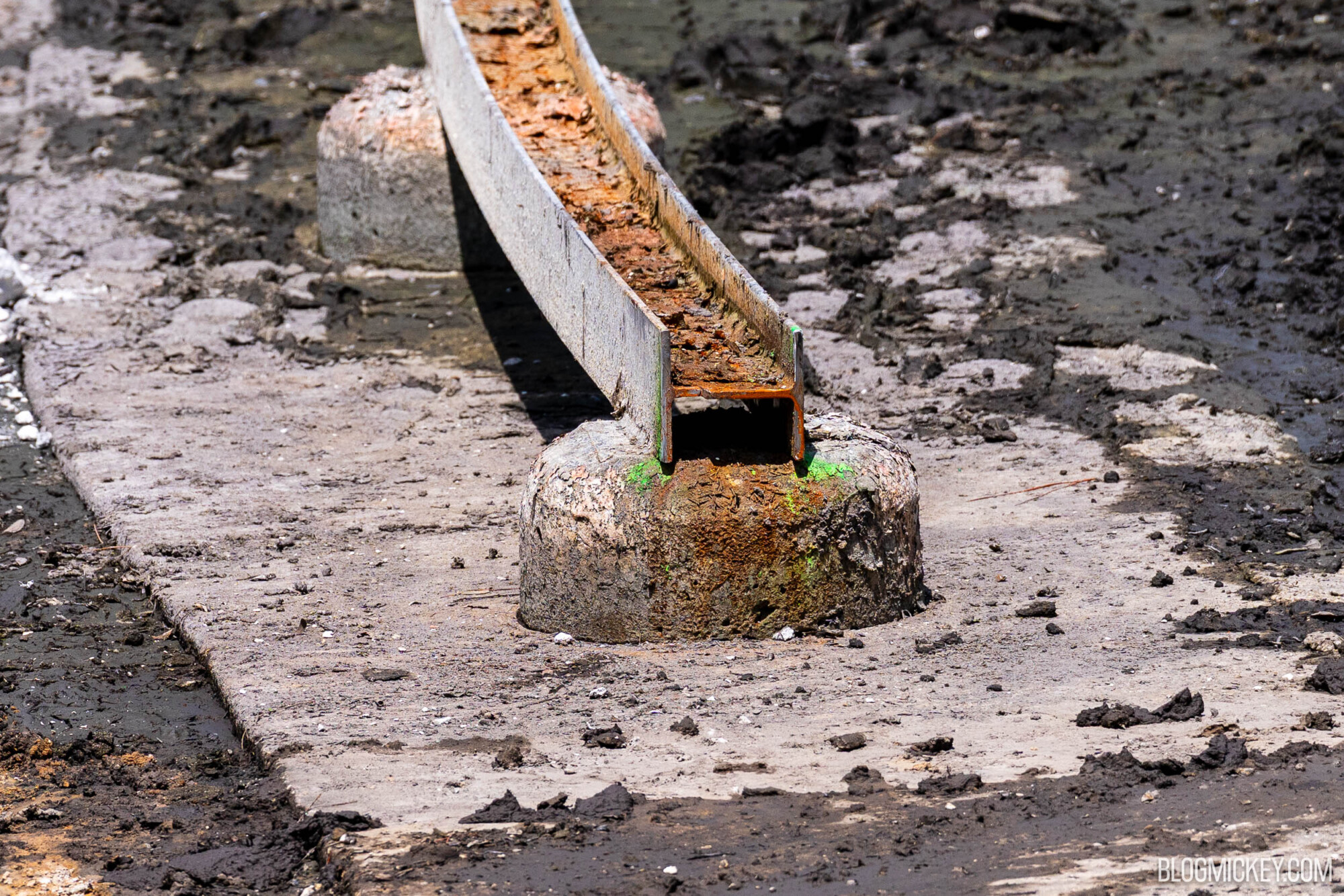 A close view of a metal track that has been cut. It is supported by a concrete pad underneath it in the drained Rivers of America