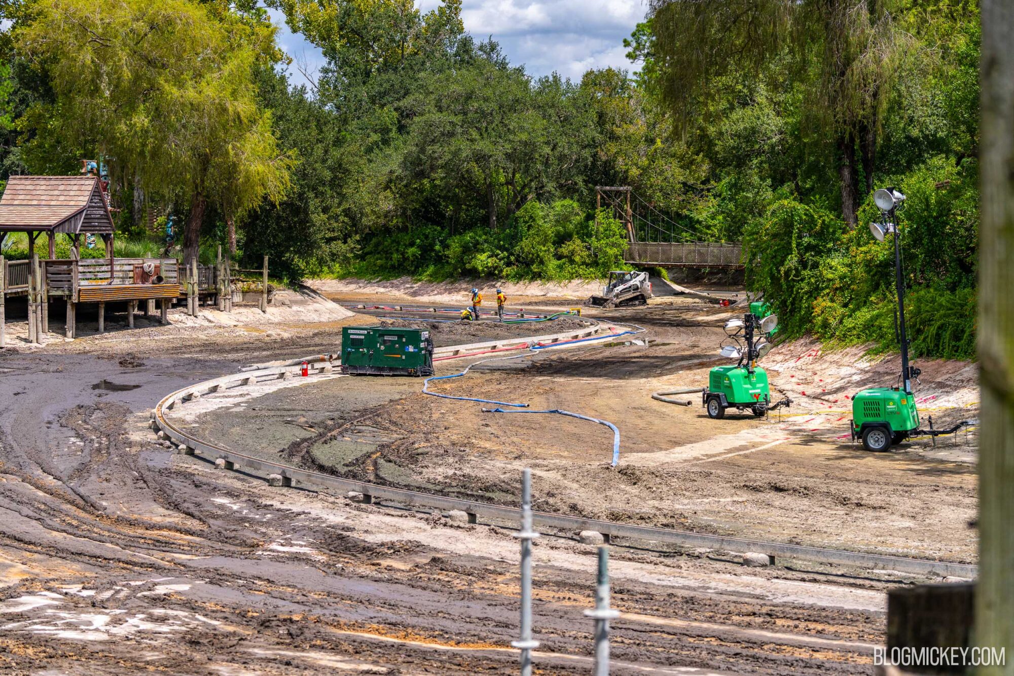 A wide view of the drained Rivers of America in Magic Kingdom with industrial water pumps and construction workers in the distance. Surrounded by lush trees